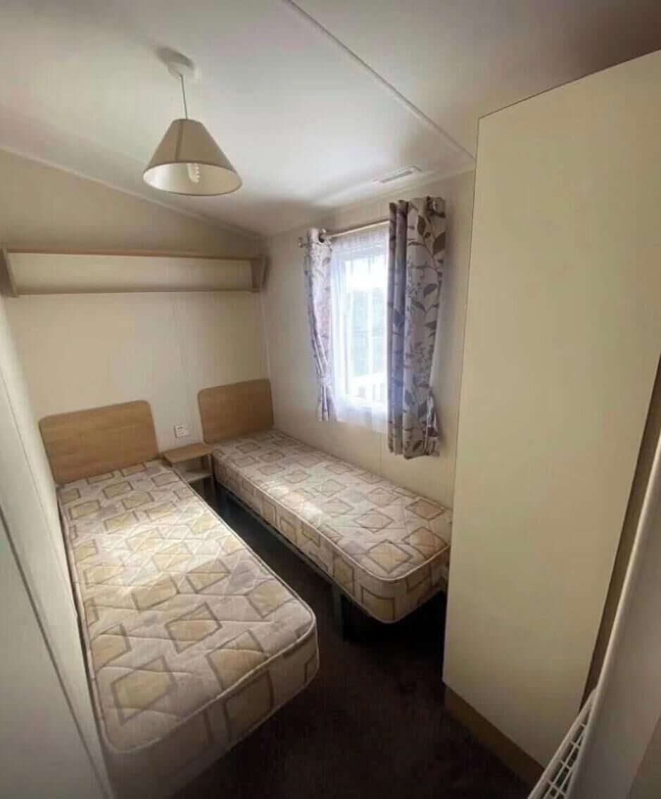 A small room with two single beds, a ceiling light, and a window with curtains.
