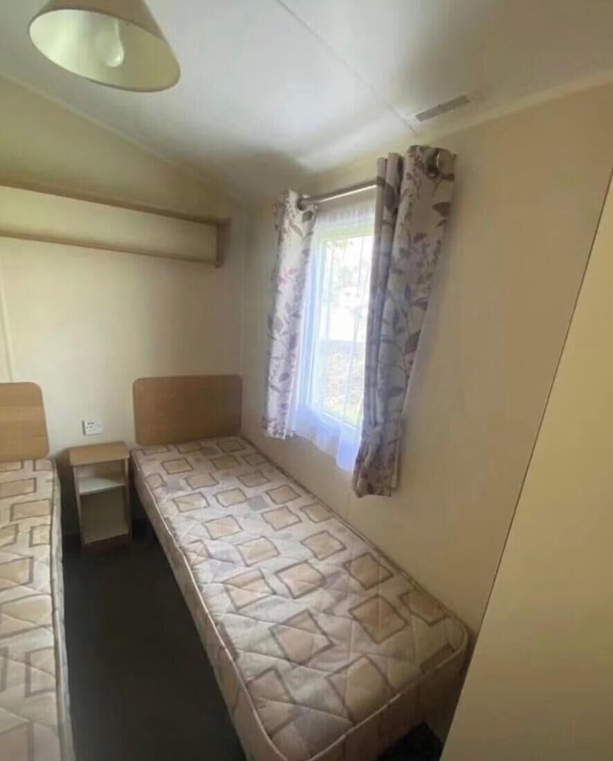 A single bed with a headboard, a small bedside table, and a window with curtains.