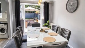Uma área de refeições com mesa branca, seis cadeiras e um relógio na parede.