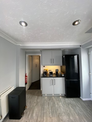 Une cuisine de taille réduite avec des meubles blancs, un réfrigérateur noir et un plancher en bois.