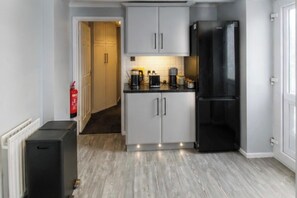 Eine kleine Küche mit weißen Schränken, einem schwarzen Kühlschrank und einer Kaffeemaschine auf der Arbeitsplatte.