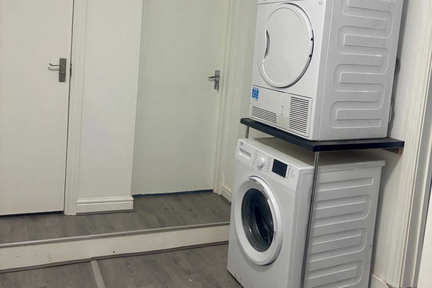 A laundry room with a front-loading washer and dryer stacked on a shelf.