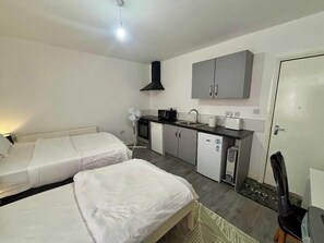 Ett kompakt hotellrum med två sängar, ett litet kök och en dörr.