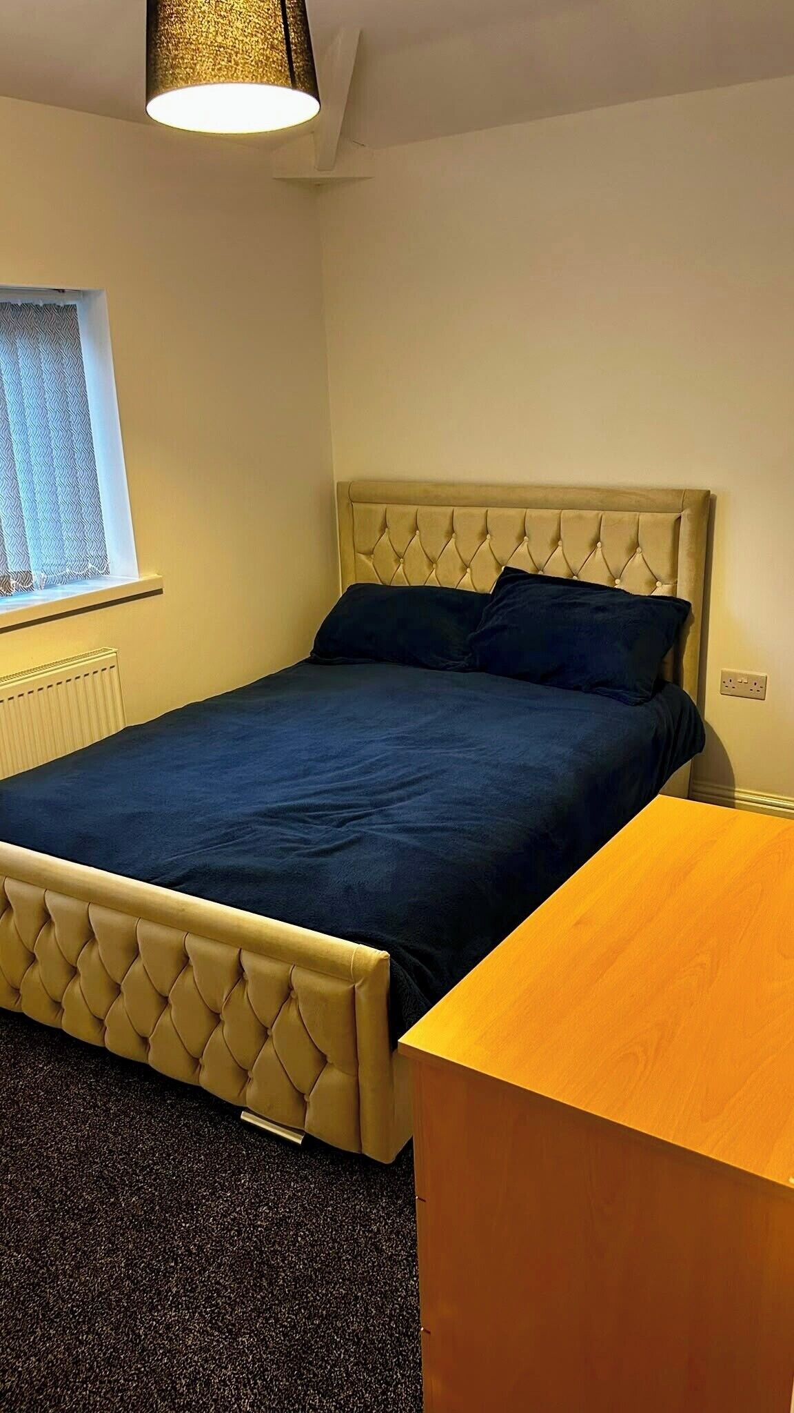 Ein Schlafzimmer mit einem Bett, einem Nachttisch, einem Fenster mit Vorhang und einer Heizung.