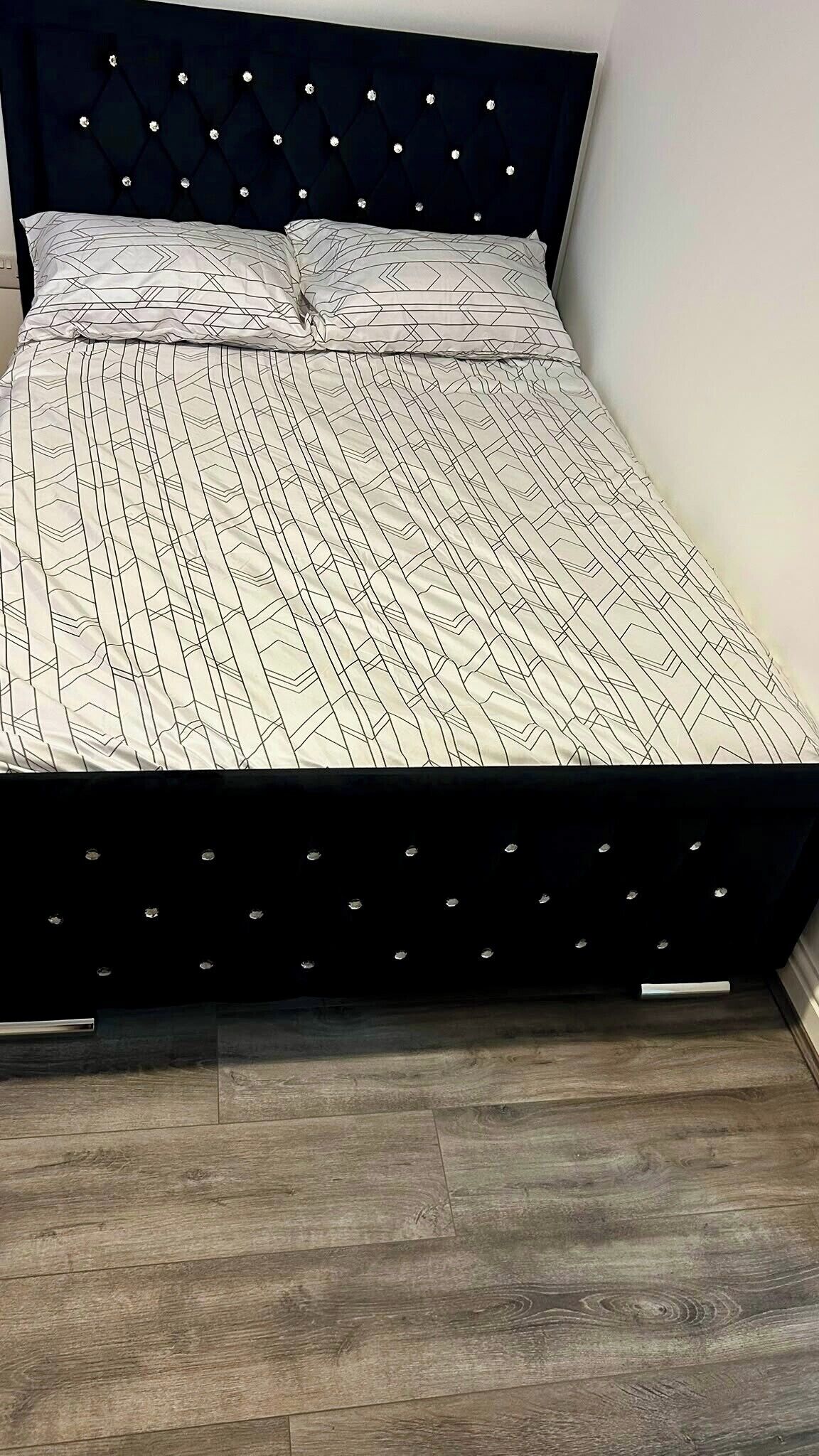 Ein Bett mit einem geometrisch gemusterten Überwurf und einem gesteppten Kopfteil mit dekorativen Elementen.