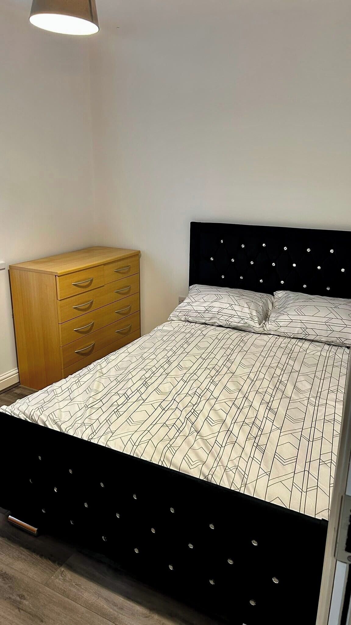 Ein Schlafzimmer mit einem Bett, einer Holzkommode und einer Deckenleuchte.