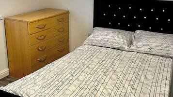 Ein Schlafzimmer mit einem Bett, einer Holzkommode und einer Deckenleuchte.