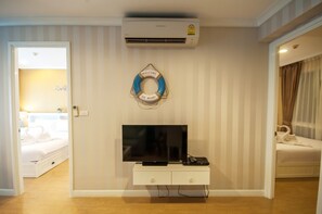 Quarto de hotel com televisão de tela plana sobre um console branco, um boia decorativo na parede e uma cama com roupa de cama branca.