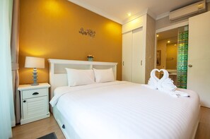 A hotel room with a bed, a nightstand, a lamp, a wall decoration, and a mirror. - A105 Cozy 2-bedroom apartment with AC in a pleasant location (Huahin)