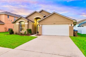 A residential house with a garage, a well-maintained lawn, and a clear sky. - Luxury 4-bedroom house for family fun, Pool, 10 mins to Disney (Kissimmee)