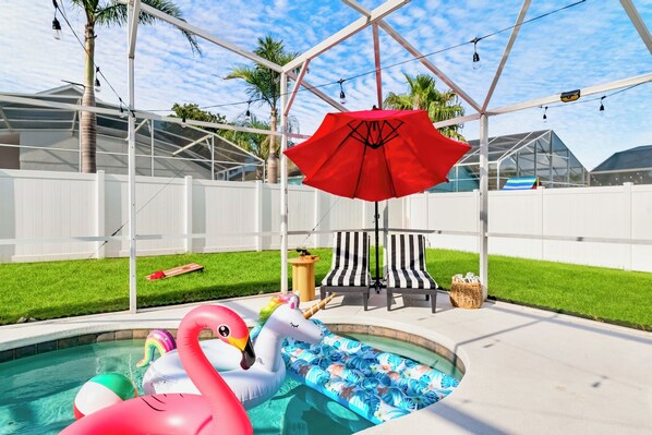 Ein Swimmingpool mit Schwimmspielzeug, einem roten Sonnenschirm und einem weißen Zaun.