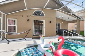 Ein überdachter Außenbereich mit Pool, einer aufblasbaren Schwane und einem Flamingo, einer Hängematte sowie einer Sitzgelegenheit mit Blick auf den Pool.