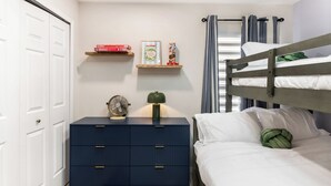 A bedroom with a bunk bed, a bedside table with a lamp, a dresser, and shelves with board games. - Luxury 4-bedroom house for family fun, Pool, 10 mins to Disney (Kissimmee)