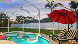 A pool area with a covered patio, lounge chairs, and a red umbrella. - Luxury 4-bedroom house for family fun, Pool, 10 mins to Disney (Kissimmee)