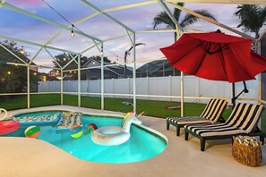 Ein Poolbereich mit überdachter Terrasse, Liegest ühlen und einem roten Sonnenschirm.