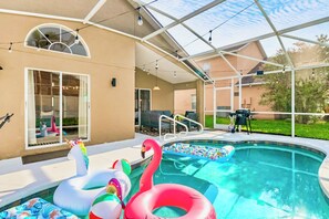 A swimming pool with inflatable swan and unicorn floats, a covered patio area, and a glass-enclosed structure. - Luxury 4-bedroom house for family fun, Pool, 10 mins to Disney (Kissimmee)
