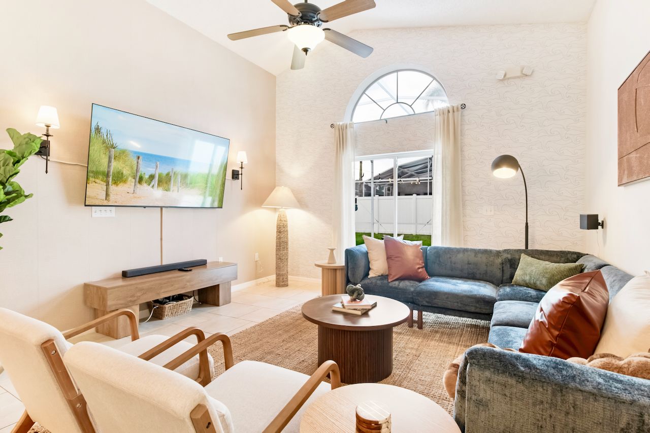 A living room with a flat-screen TV, a ceiling fan, a sofa, a coffee table, and a large window with curtains.