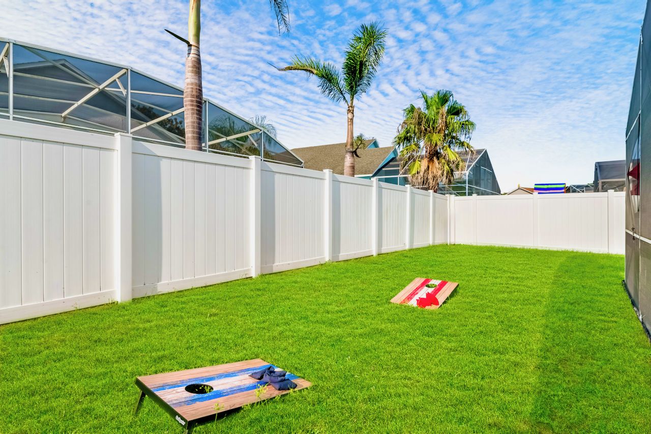 A backyard with a white fence, a palm tree, and a wooden deck.