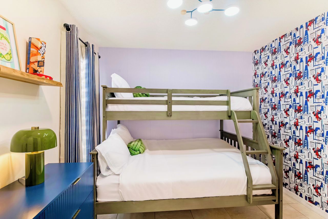 A bunk bed with a ladder, a bedside table with a lamp, and a wall with patterned wallpaper.