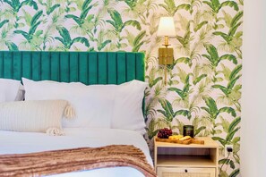 Une chambre d’hôtel avec un lit, une table de chevet, une lampe et un papier peint aux motifs tropicaux.
