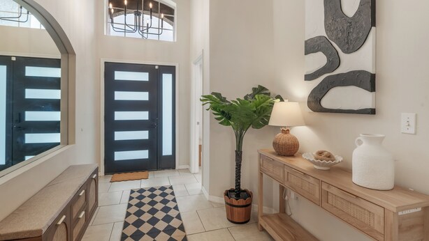 A modern interior with a checkered floor, a potted plant, a console table with decorative items, and a large abstract wall art piece. - Luxury 4-bedroom house for family fun, Pool, 10 mins to Disney (Kissimmee)