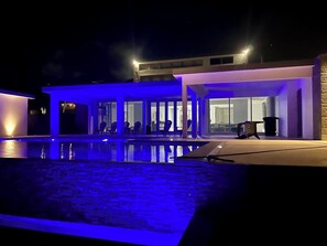Ein moderner Poolbereich mit überdachter Lounge und einem Gebäude im Hintergrund.