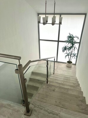 Eine Treppe mit Glastrennwand, die zu einem Raum mit einem großen Fenster und einem Blumentopf führt.