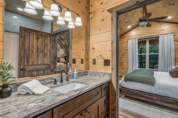 A wooden cabin interior with a bathroom featuring a large mirror, a sink, and a shower. - Happy Chipmunk - Mountain Views, Hot Tub, Fire Pit & Game Room (Sevierville)