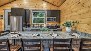 A kitchen with a wooden ceiling, a large window, and a dining area with a marble countertop and chairs. - Happy Chipmunk - Mountain Views, Hot Tub, Fire Pit & Game Room (Sevierville)