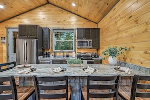 A kitchen with a wooden ceiling, a large window, and a dining area with a marble countertop and chairs. - Happy Chipmunk - Mountain Views, Hot Tub, Fire Pit & Game Room (Sevierville)