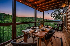 A wooden deck with a table set for dining, overlooking a forested landscape. - Happy Chipmunk - Mountain Views, Hot Tub, Fire Pit & Game Room (Sevierville)