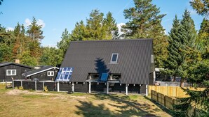 Une maison moderne à deux étages, dotée d’un toit en pente, de panneaux solaires et d’une cour clôturée.