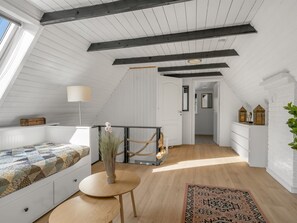 A loft bedroom with a sloped ceiling, a bed with a patterned quilt, a small round table with a vase, a hanging chair, and a view of the hallway. - "Ilsebeth" -  from the sea by Interhome (Hals)