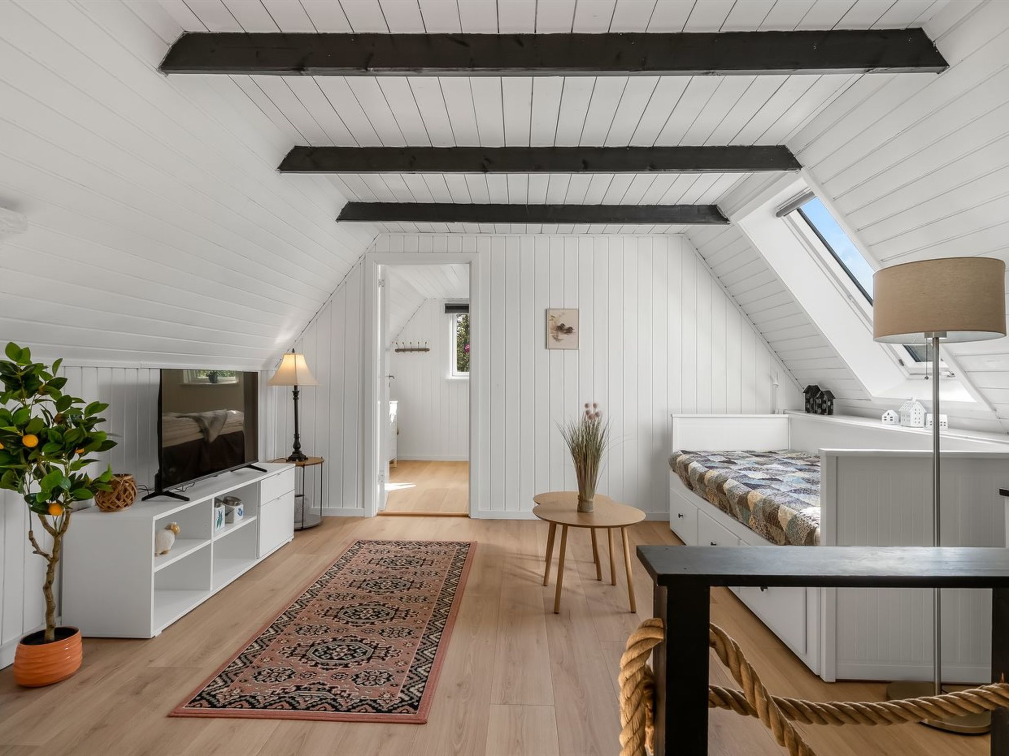 A loft-style room with a sloped ceiling, a television, a dining table, and a sofa.