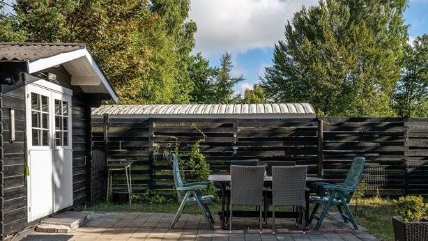 Une terrasse avec un sol en briques, une table avec des chaises et un petit abri de jardin avec une porte.
