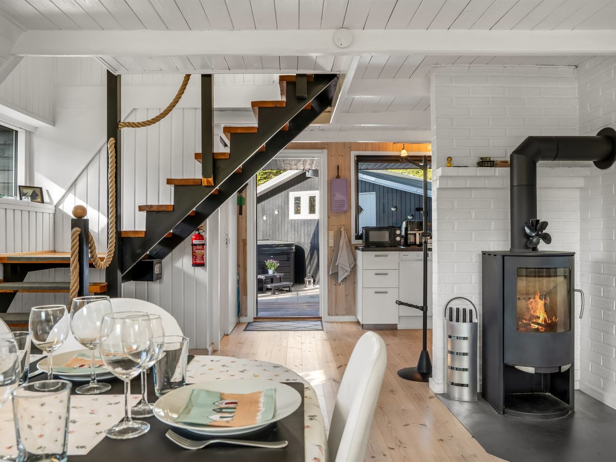A modern kitchen with a built-in wood stove, a dining area with a table set for four, and a staircase with a wooden handrail.