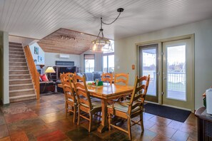 A dining area with a wooden table and chairs, a staircase, and a view through a glass door.