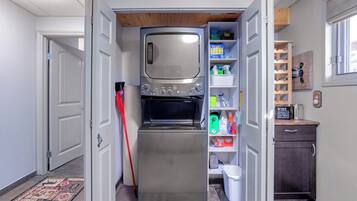 A compact kitchen with a built-in oven and microwave, a small pantry with storage shelves, and a wooden ceiling.