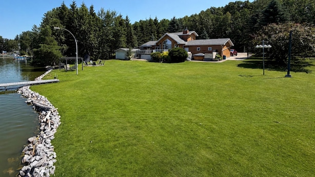 En ejendom ved søen med velholdt græsplæne, en anløbsbro og et hus med stor terrasse.