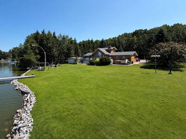 A house with a well-maintained lawn, a dock, and a forested area in the background.