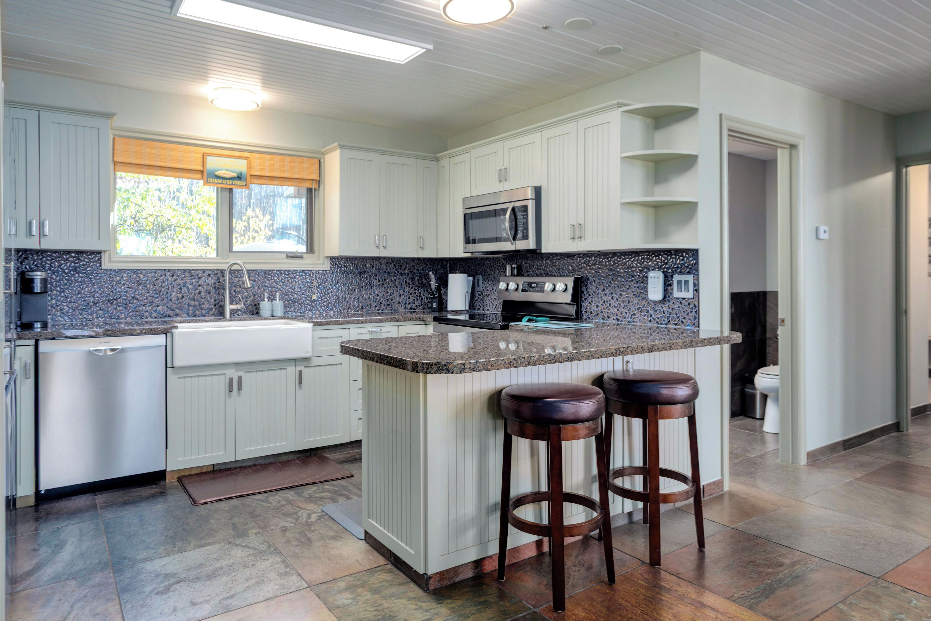 A modern kitchen with white cabinets, a granite countertop, a built-in microwave, and a stainless steel refrigerator.