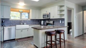 A modern kitchen with white cabinets, a granite countertop, a built-in microwave, and a stainless steel refrigerator.