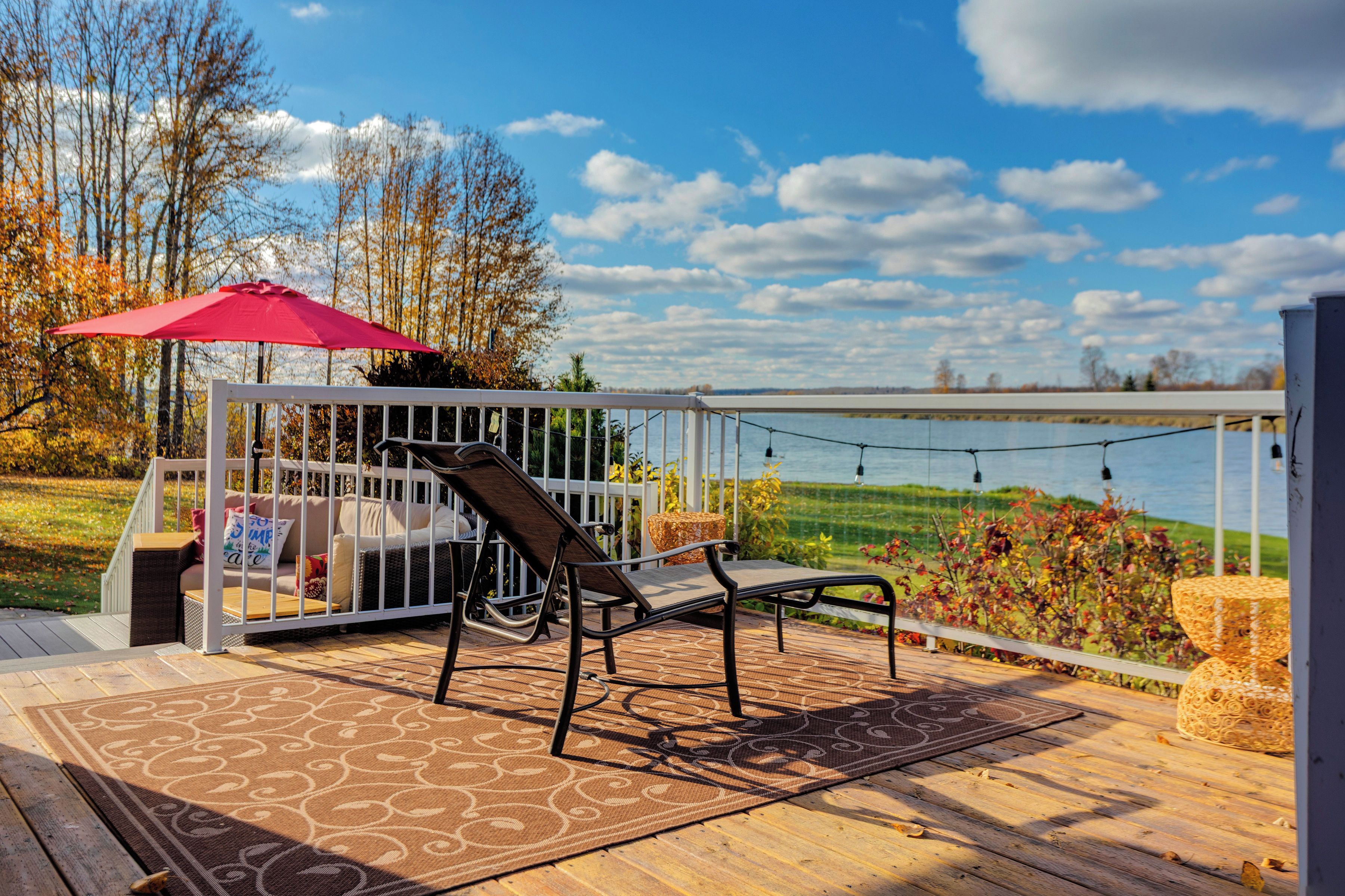 A deck with a chair and umbrella, overlooking a body of water and trees.