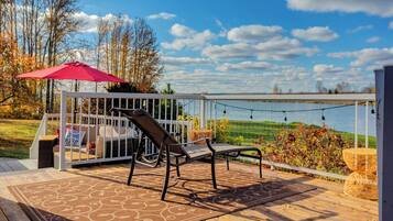 A deck with a chair and umbrella, overlooking a body of water and trees.