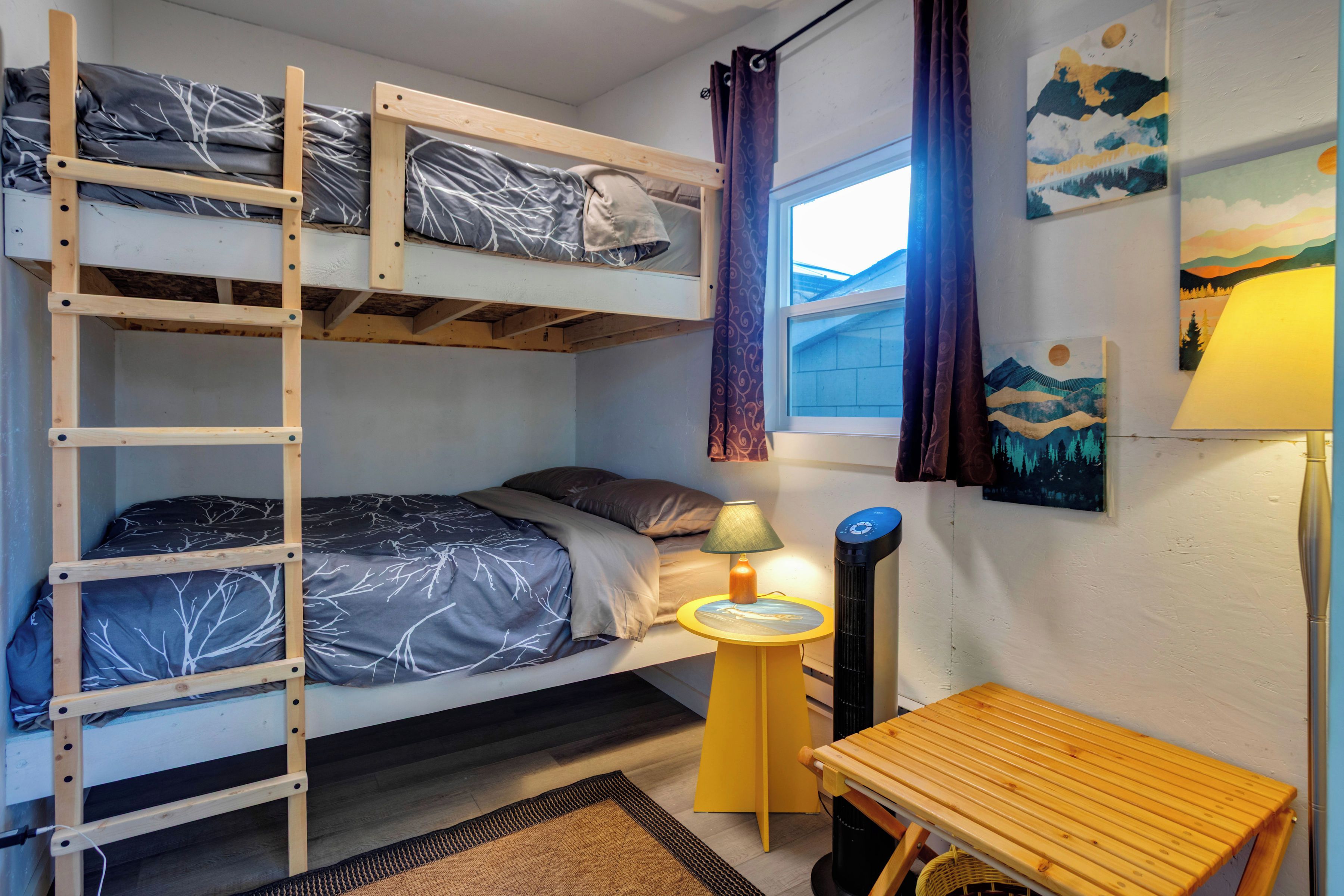 Een stapelbed met een ladder, een nachtkastje met een lamp en een raam met gordijnen.