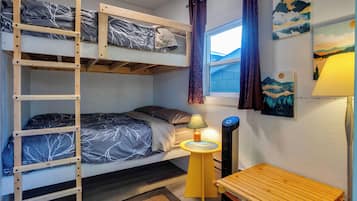 A bunk bed with a ladder, a bedside table with a lamp, and a window with curtains.
