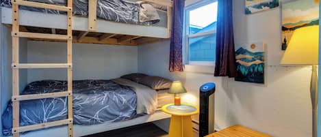 Een stapelbed met een ladder, een nachtkastje met een lamp en een raam met gordijnen.