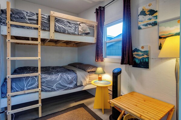 A bunk bed with a ladder, a bedside table with a lamp, and a window with curtains.
