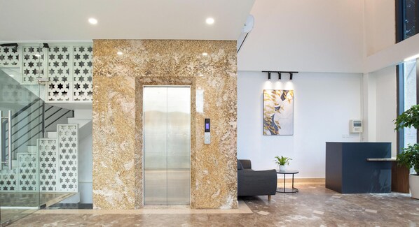 Un hall d’entrée moderne avec un ascenseur en marbre, un comptoir d’accueil, un escalier et un espace détente.