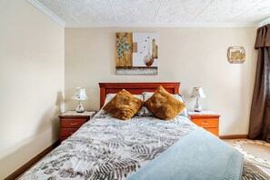 Ein Schlafzimmer mit einem Bett, zwei Nachttischen, einem Holzkopfende, einer Wanddekoration und einer Nachttischlampe auf jeder Seite.